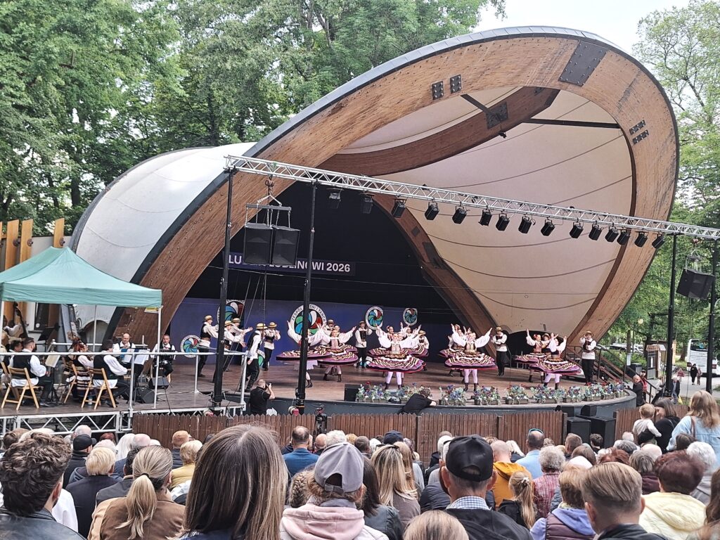 Grupa par tanecznych w kolorowych strojach ludowych tańczących na scenie w muszli koncertowej