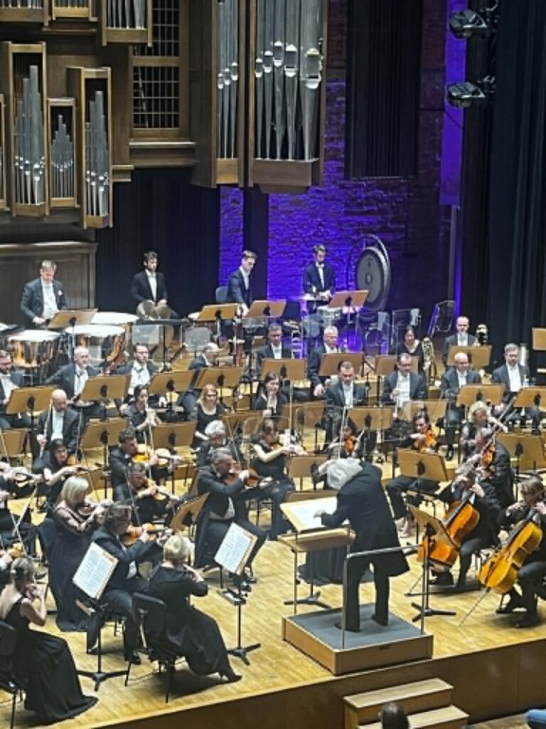 Orkiestra grająca na drewnianej scenie we wnętrzu oświetlonym w tle fioletowym światłem