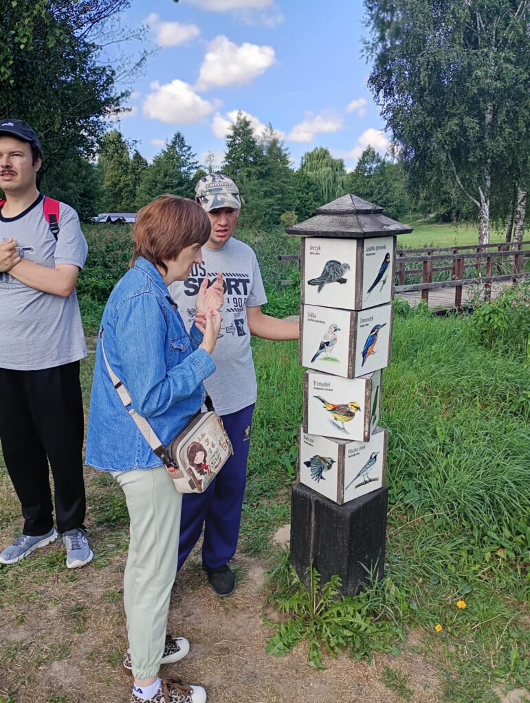 Trzy dorosłe osoby stojące przy tablicach edukacyjnych z wizerunkami i nazwami ptaków
