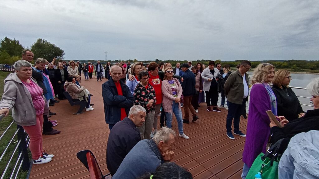 Duża grupa dorosłych osób stojących na pomoście przy rzece płynącej po prawej stronie