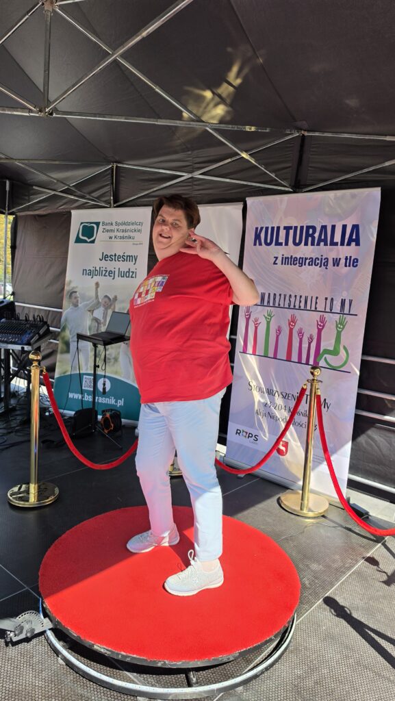 Na scenie kobieta w czerwonej koszulce stojąca na czerwonym okręgu