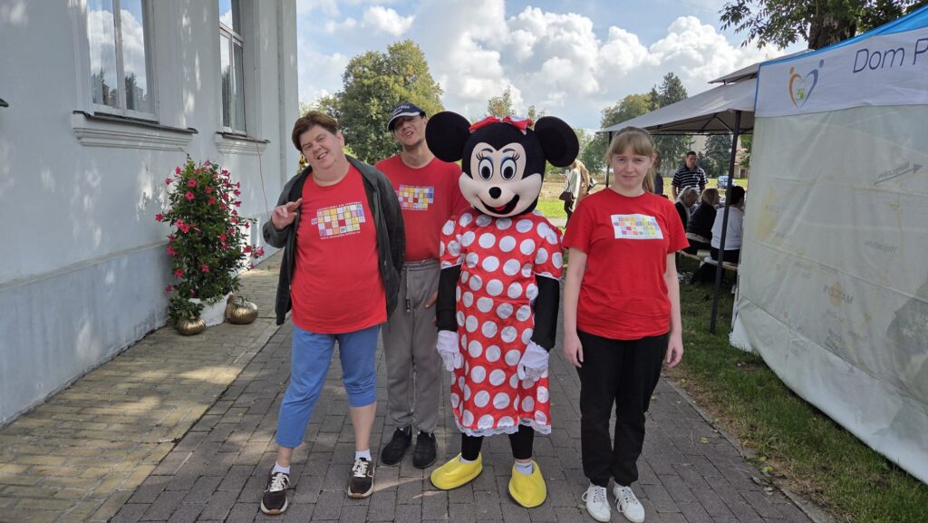 Trzy dorosłe osoby w czerwonych podkoszulkach i czwartą w stroju Myszki Minnie w czerwonej sukience w białe koła