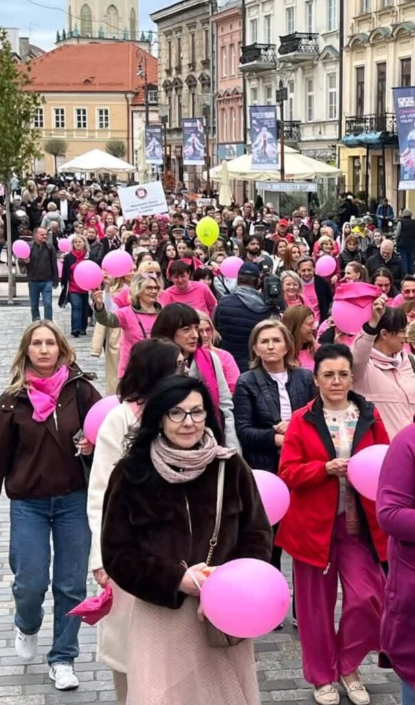 Dorosłe osoby niosące różowe balony i idące ulicą zabudowaną kamienicami