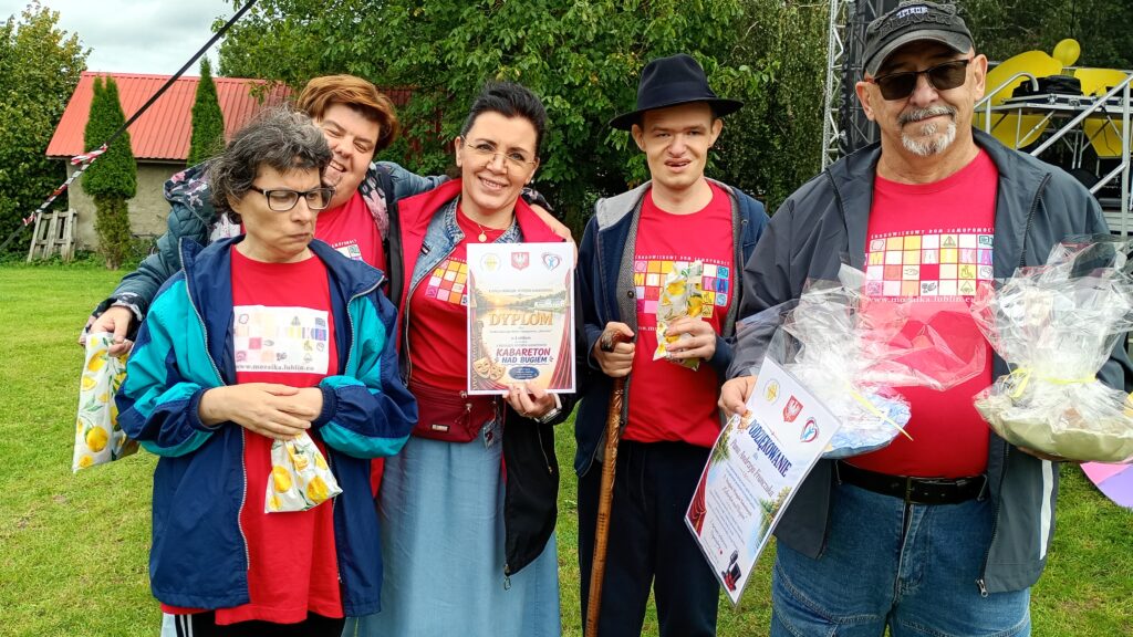 Sześć dorosłych osób w czerwonych podkoszulkach a niektóre z nich trzymają przed sobą okolicznościowe dyplomy